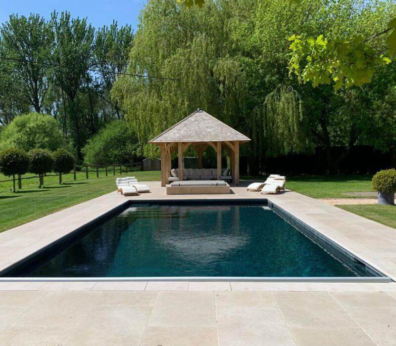 Poolcraft Ltd - An outside inground pool with a sandstone tile surround and a lounge area with a pergola